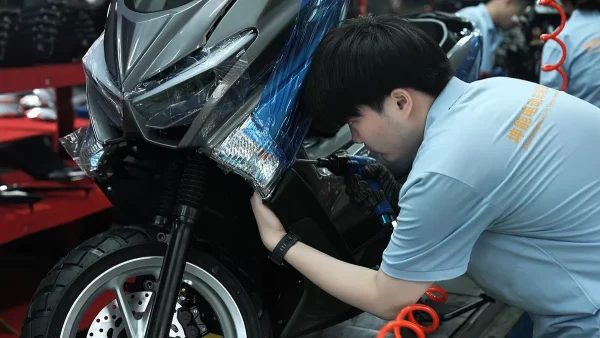 Worker assembling a blue seated electric scooter at the factory