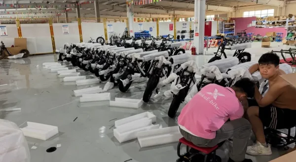 Workers fitting protective packaging around electric two-wheelers