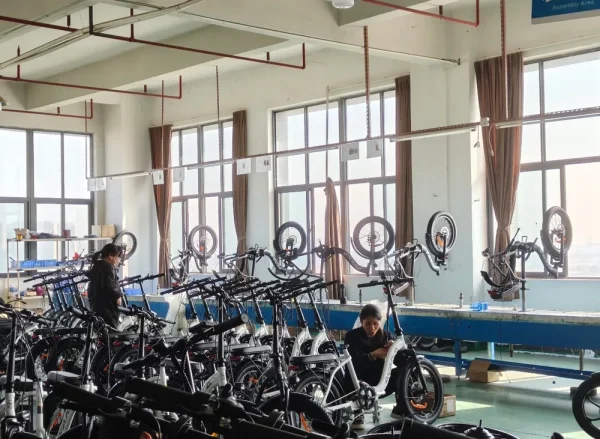Workers assembling electric bikes beside windows in a factory workshop